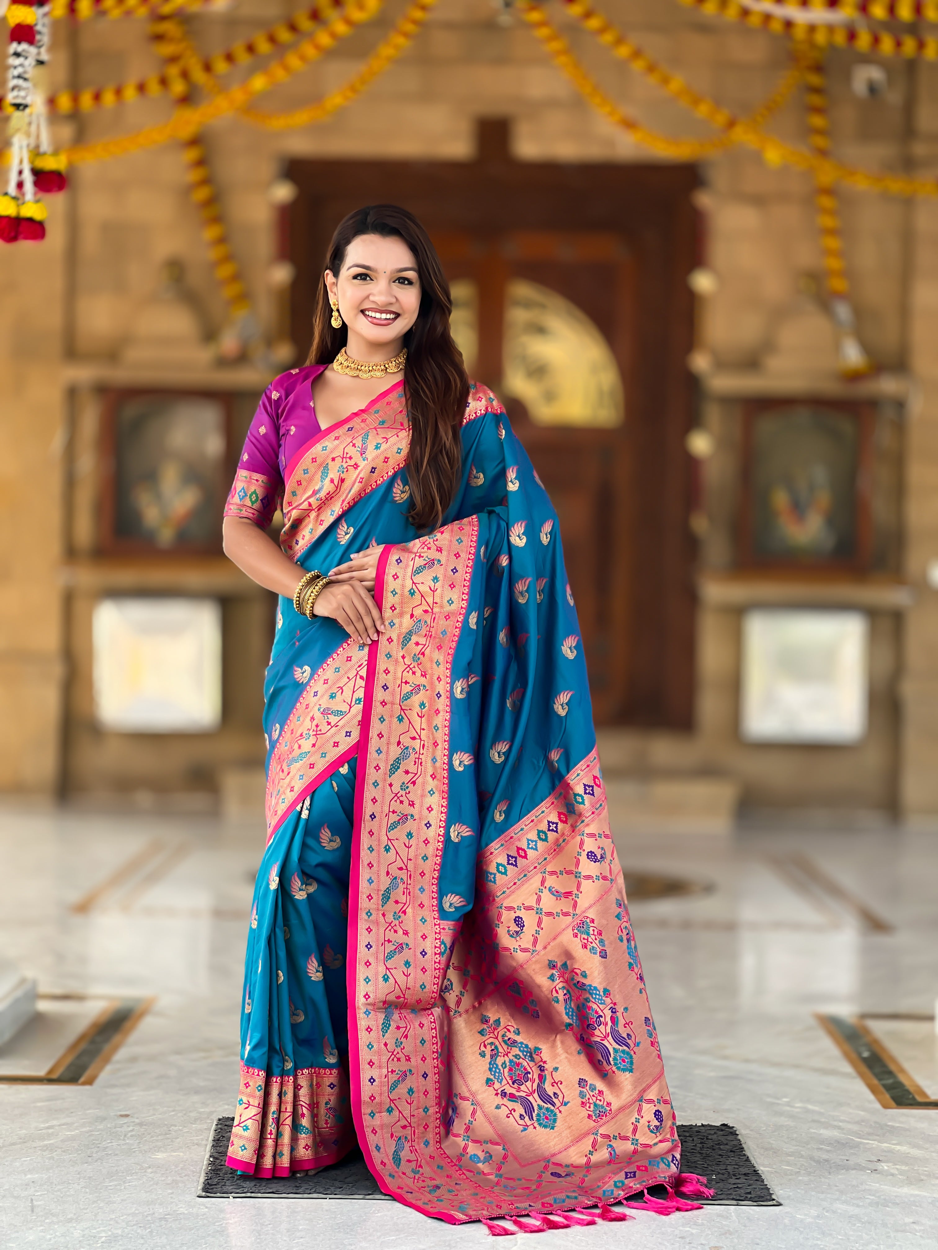 Woman wearing bottle Firozi soft Paithani silk saree with red Meenakari border and peacock zari motifs standing in a temple setting