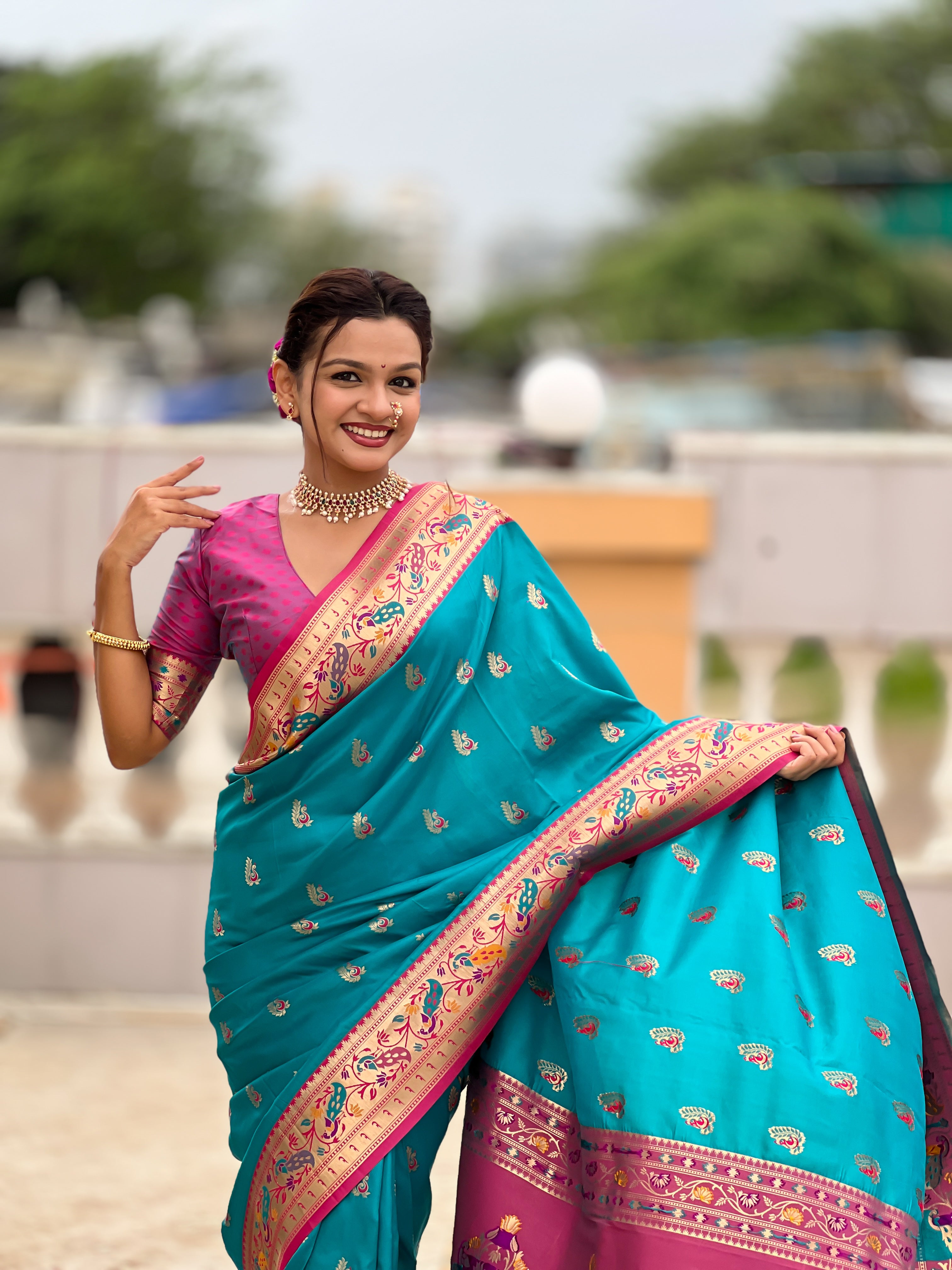 Model wearing a royal soft Paithani silk saree with Meenakari zari weaving and contrast pink border in a traditional temple setting