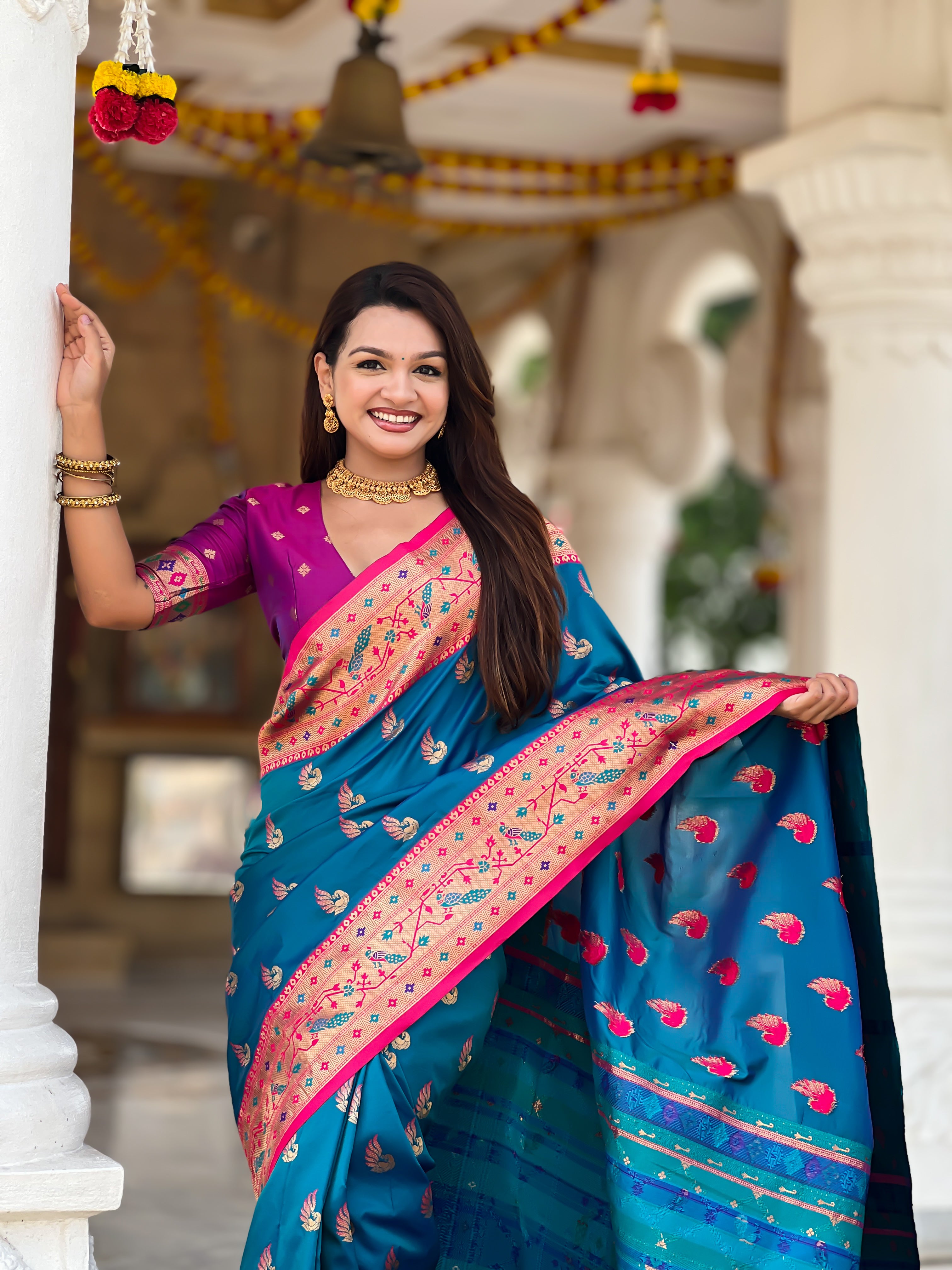 Woman wearing bottle Firozi soft Paithani silk saree with red Meenakari border and peacock zari motifs standing in a temple setting