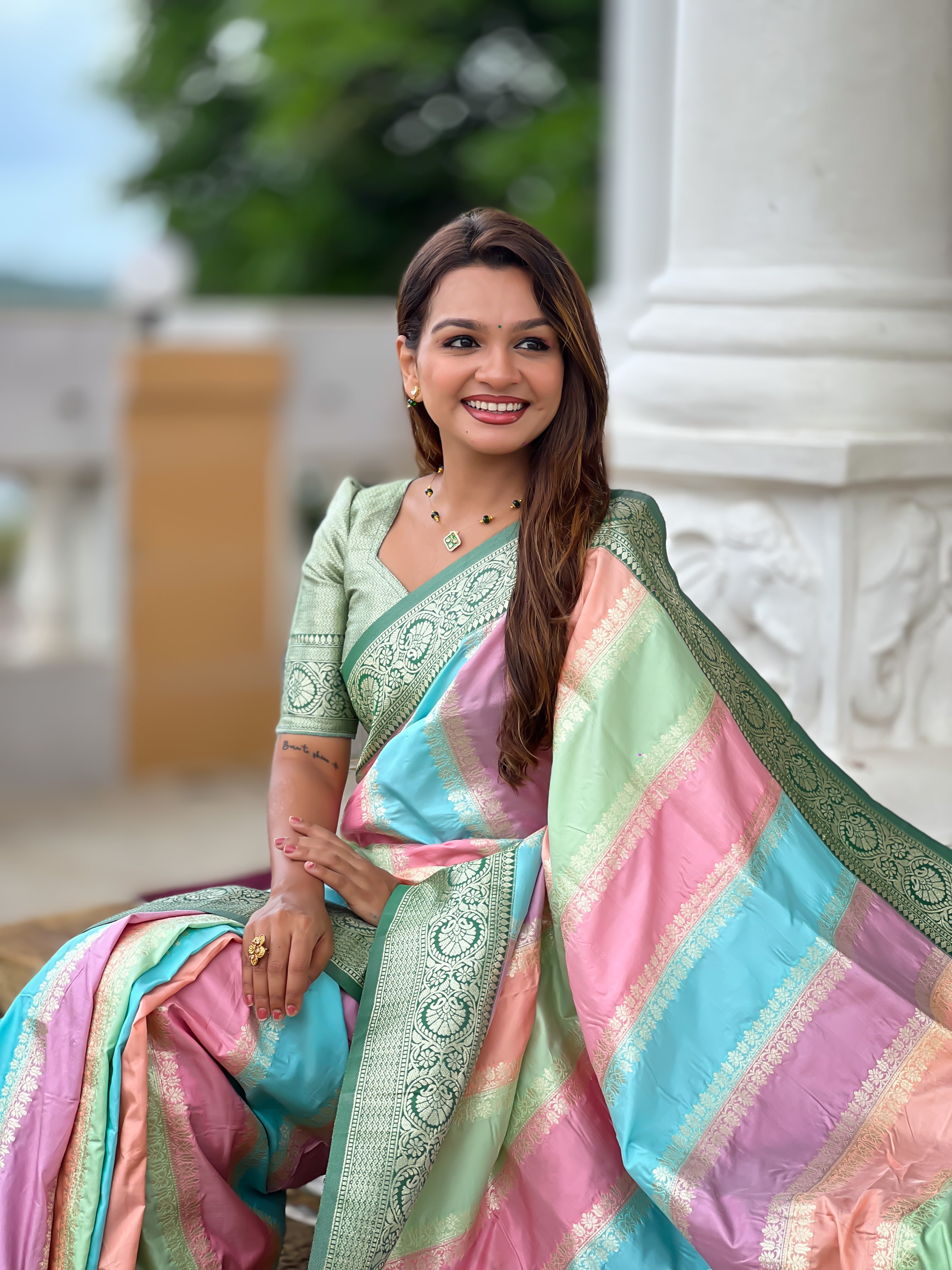 Woman wearing multi-colored pastel soft silk saree with intricate green zari border and Meenakari weaving details