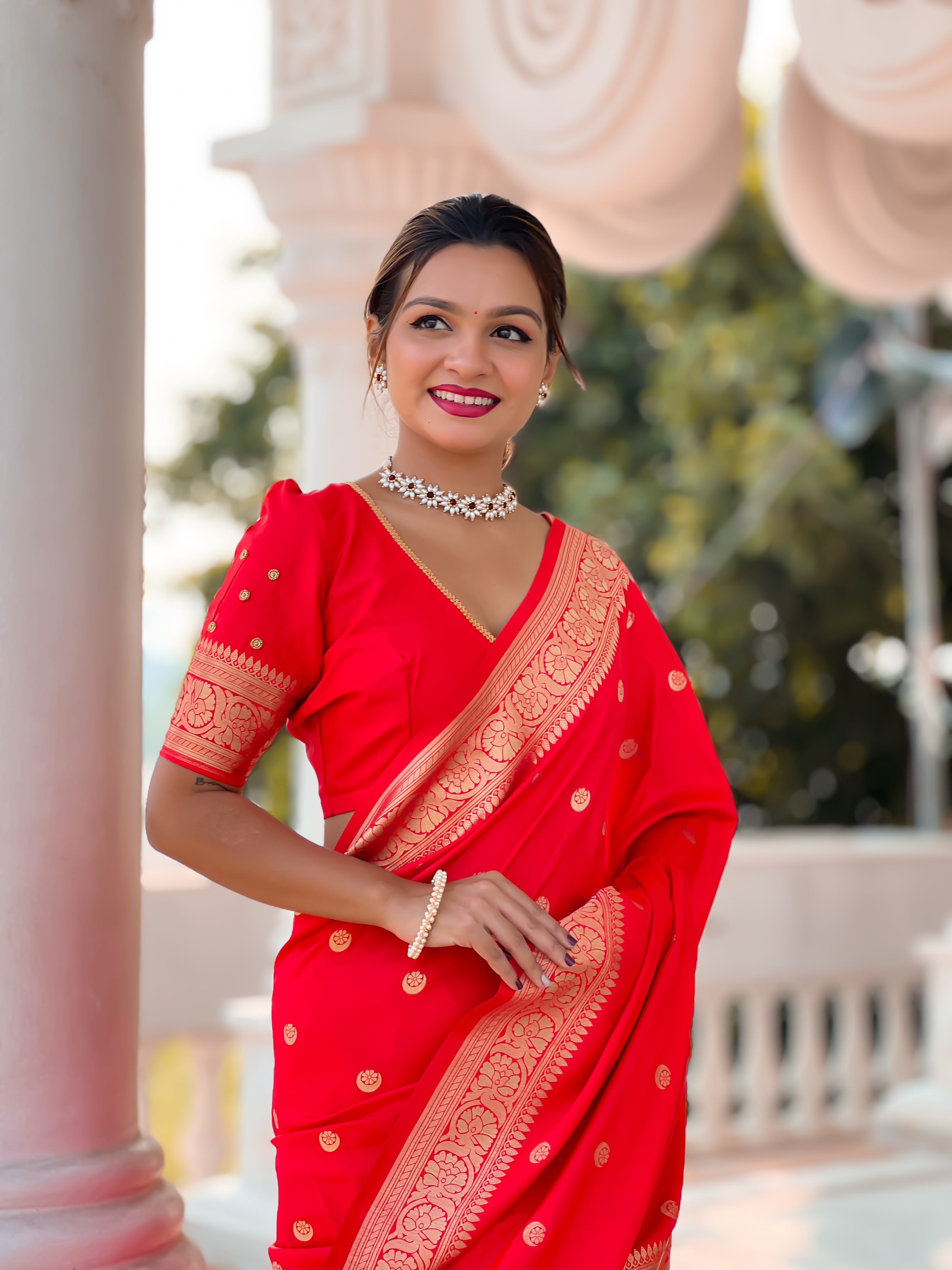 Woman wearing regal red soft Banarasi silk saree with gold zari weaving motifs and rich pallu standing in traditional setting