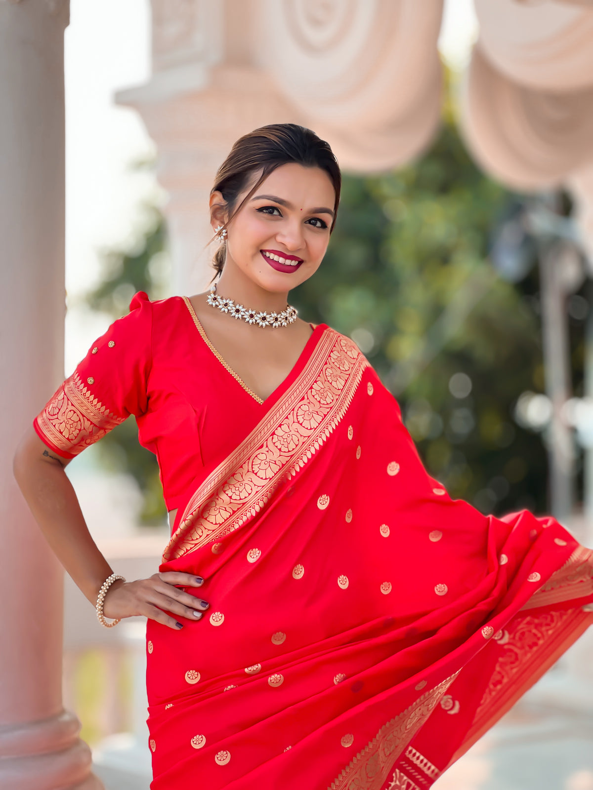 Woman wearing regal red soft Banarasi silk saree with gold zari weaving motifs and rich pallu standing in traditional setting