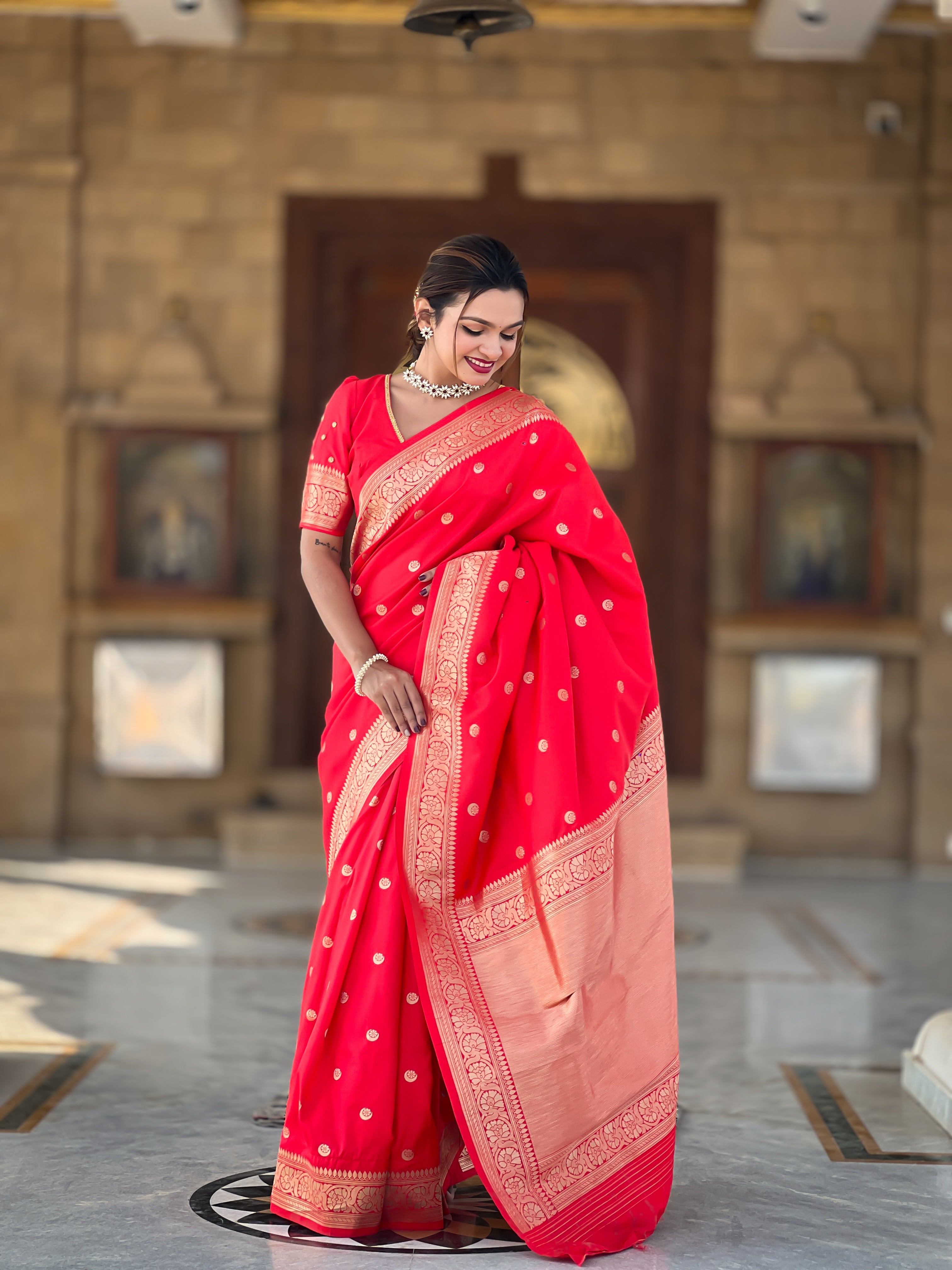 Woman wearing regal red soft Banarasi silk saree with gold zari weaving motifs and rich pallu standing in traditional setting
