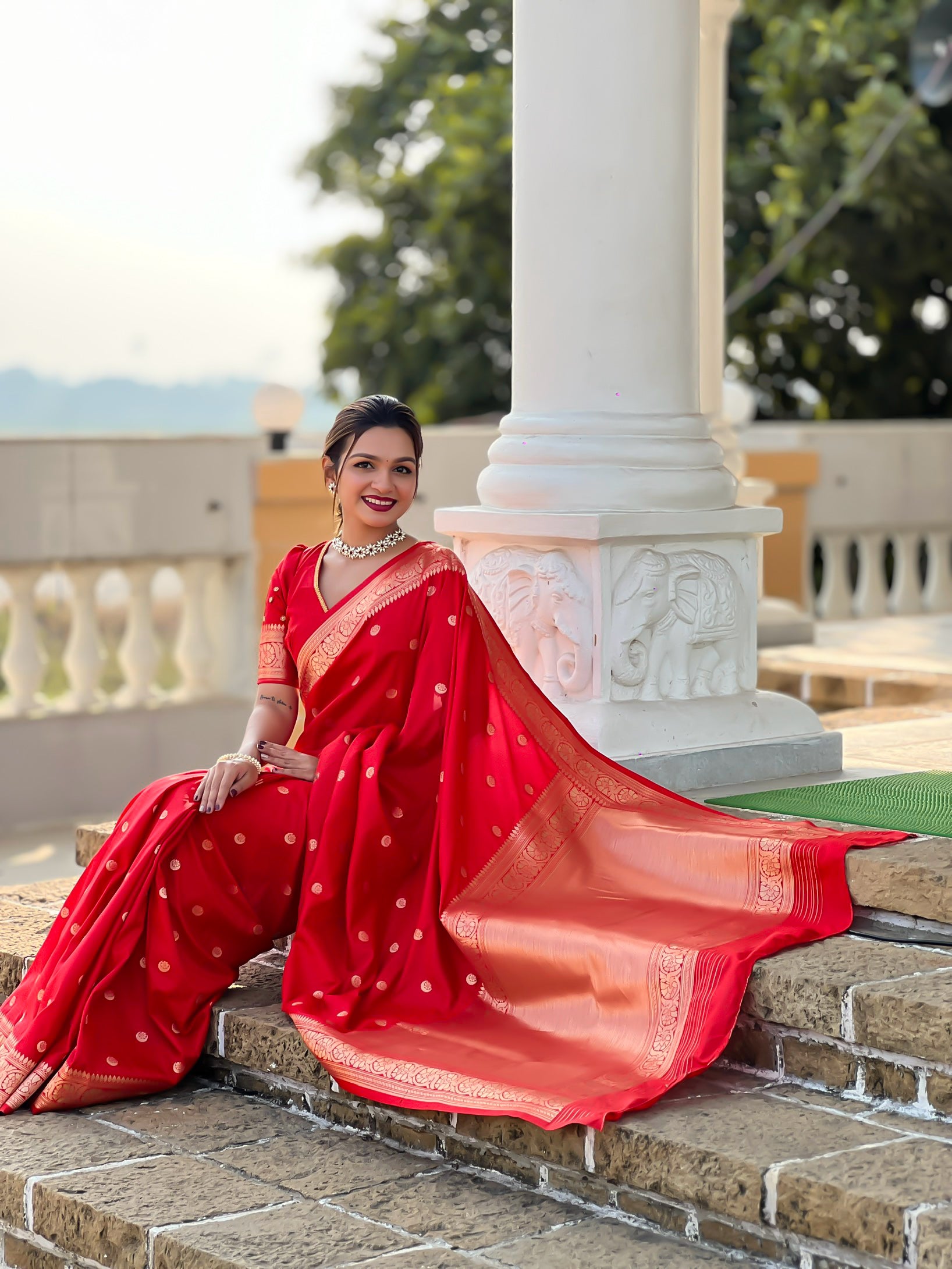 Woman wearing regal red soft Banarasi silk saree with gold zari weaving motifs and rich pallu standing in traditional setting