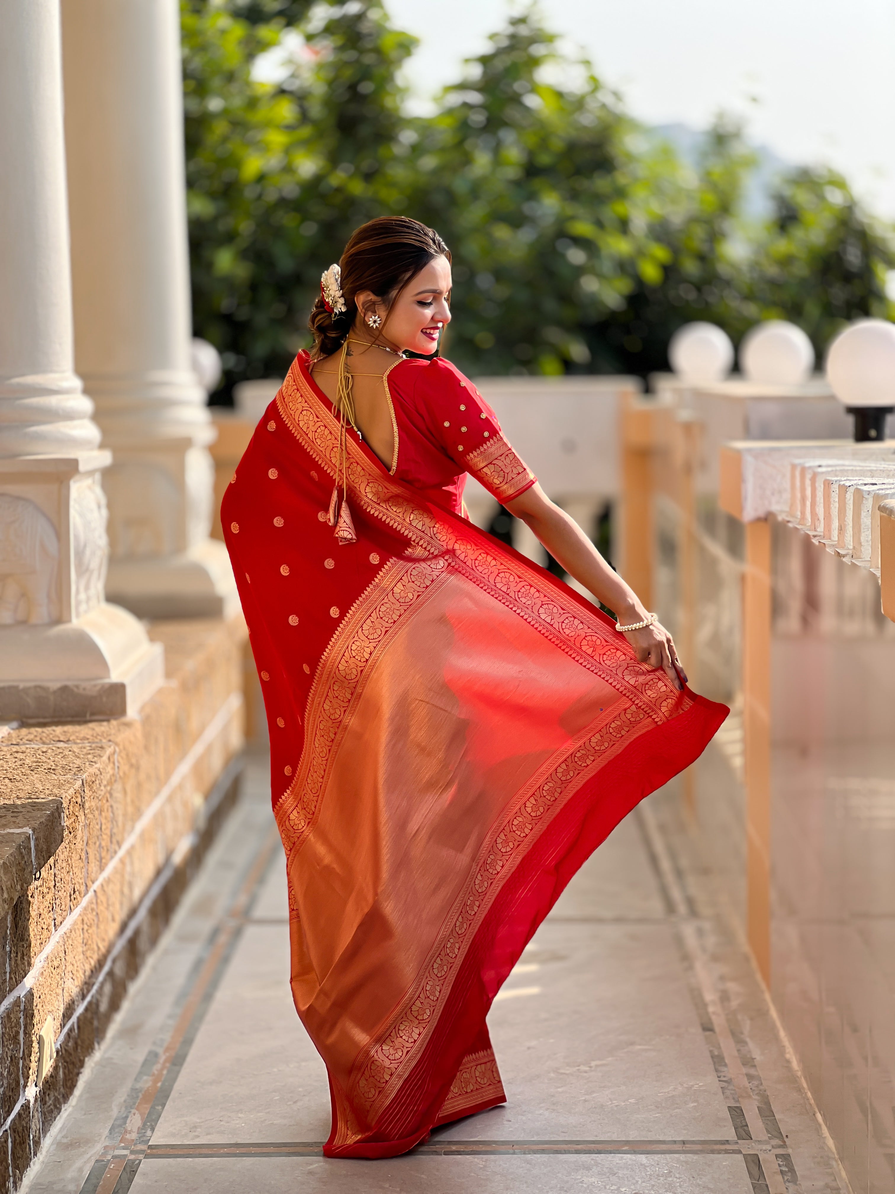 Woman wearing regal red soft Banarasi silk saree with gold zari weaving motifs and rich pallu standing in traditional setting