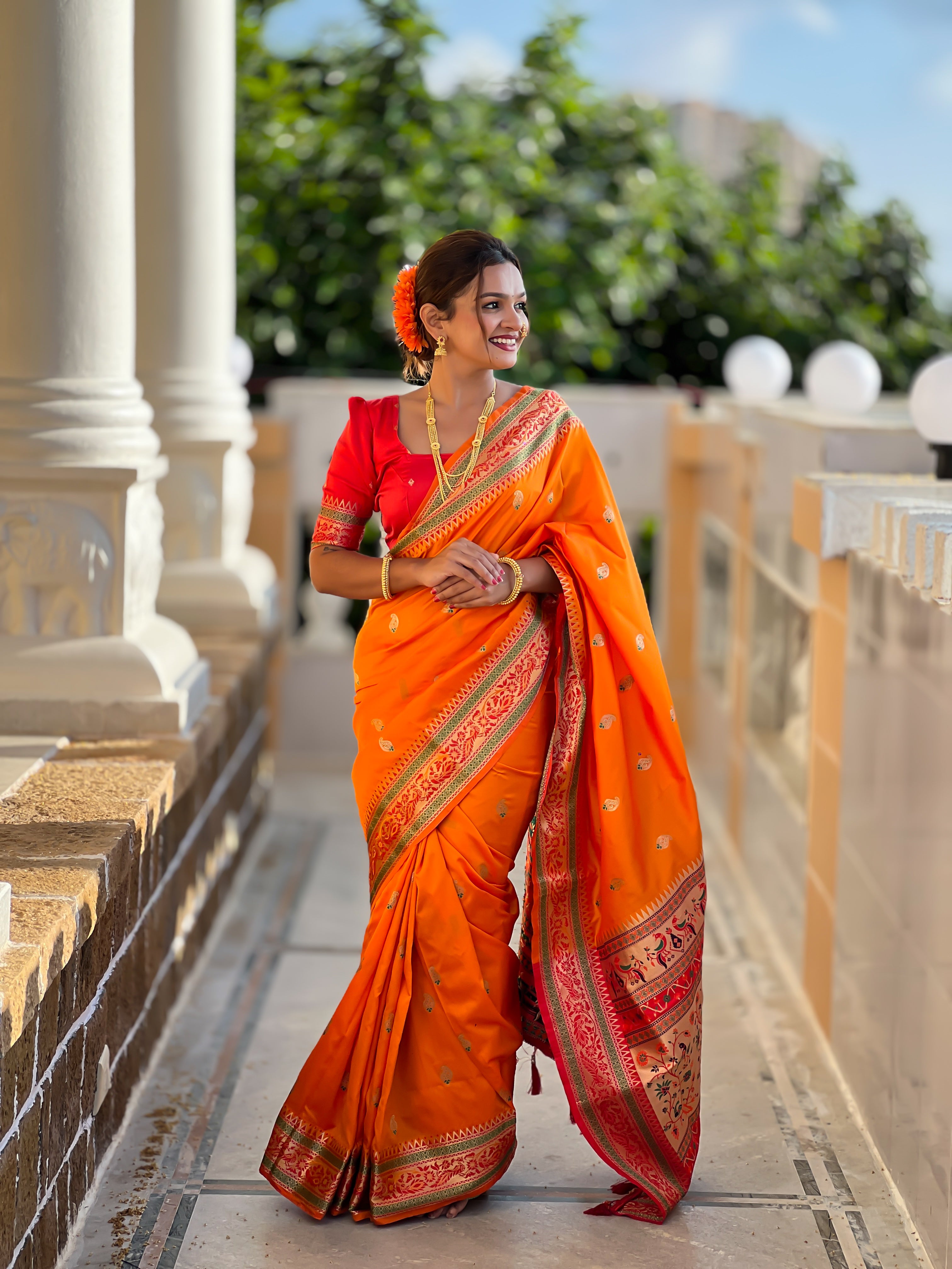 Model wearing radiant orange Soft Paithani silk saree with red border and meenakari gold zari weaving