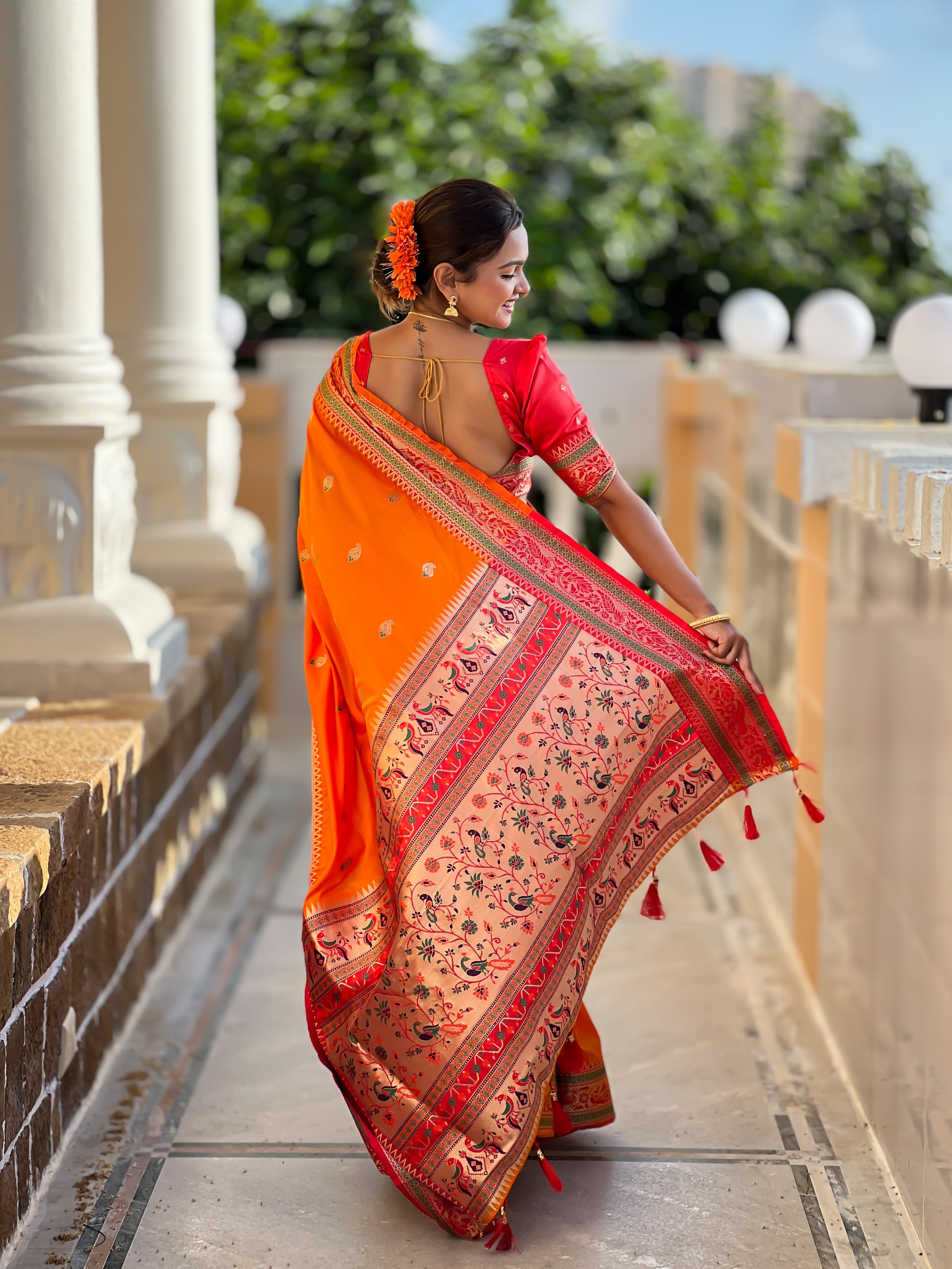 Model wearing radiant orange Soft Paithani silk saree with red border and meenakari gold zari weaving