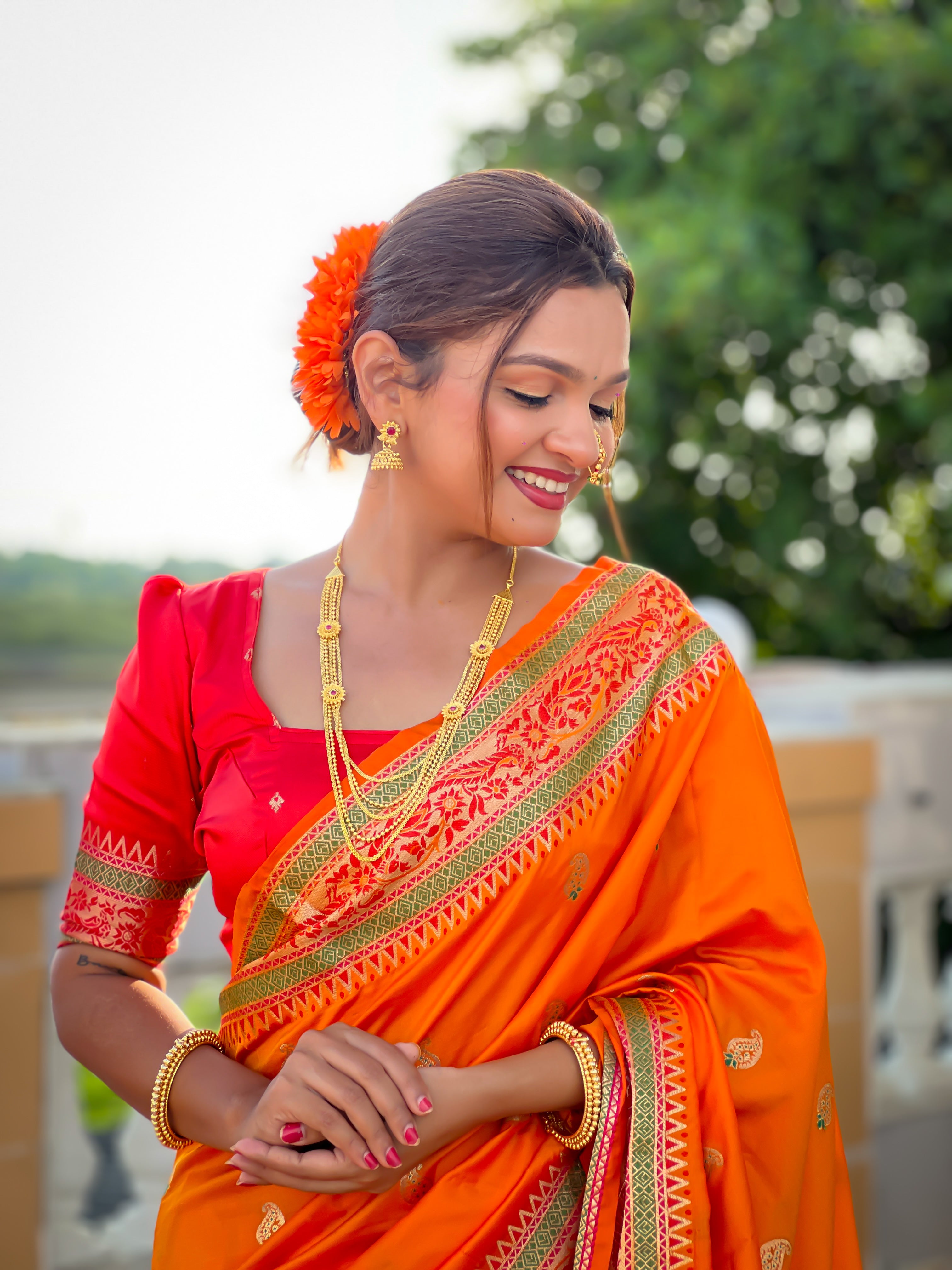 Model wearing radiant orange Soft Paithani silk saree with red border and meenakari gold zari weaving