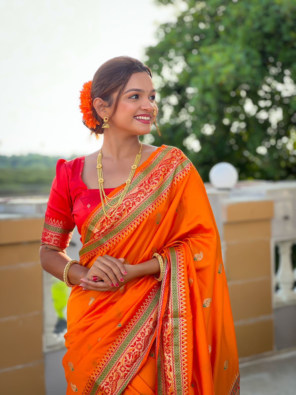 Model wearing radiant orange Soft Paithani silk saree with red border and meenakari gold zari weaving