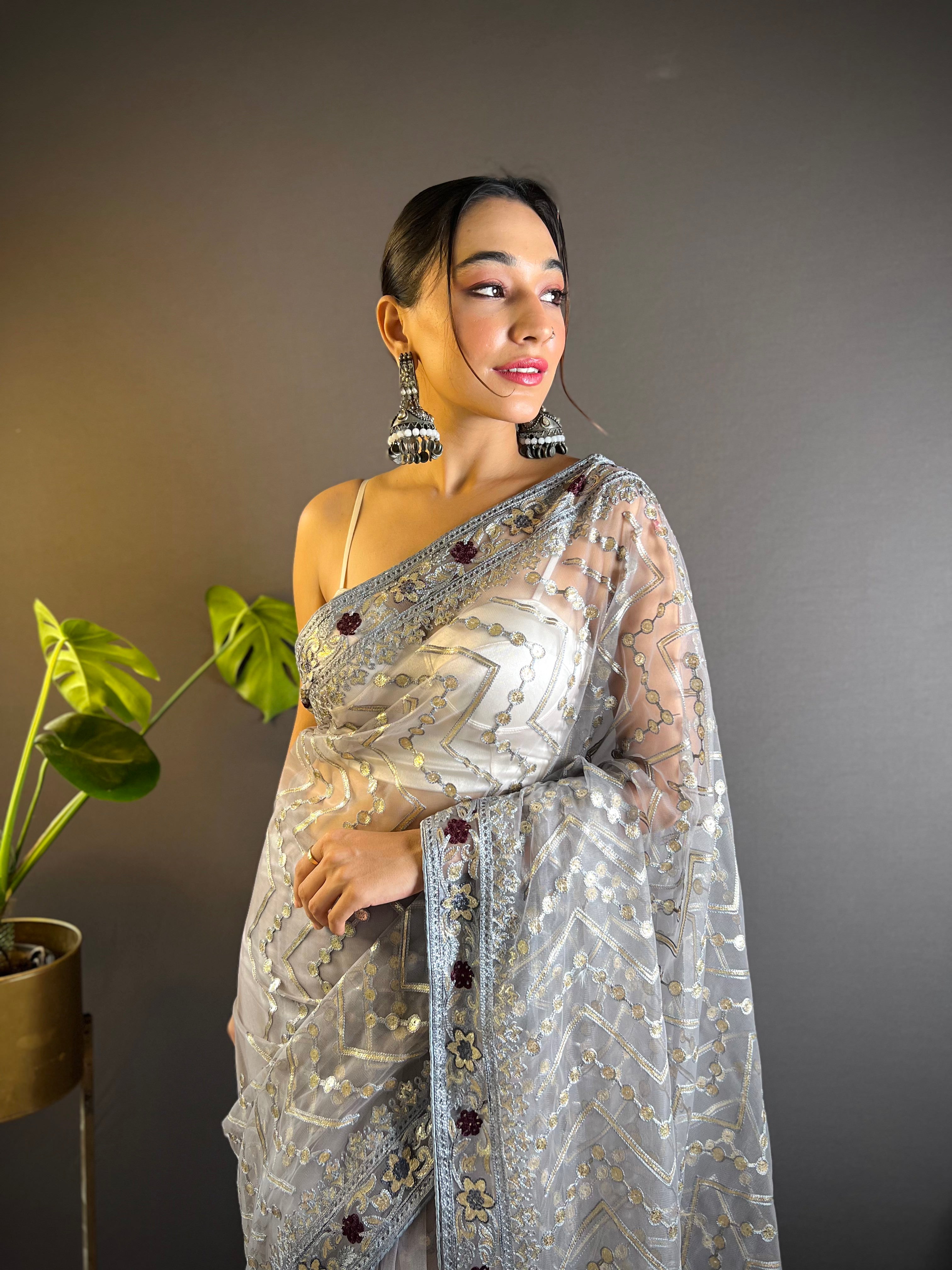 Model wearing a sheer butterfly net saree with geometric chain stitch embroidery, foil thread work, and heavy stone embellished border