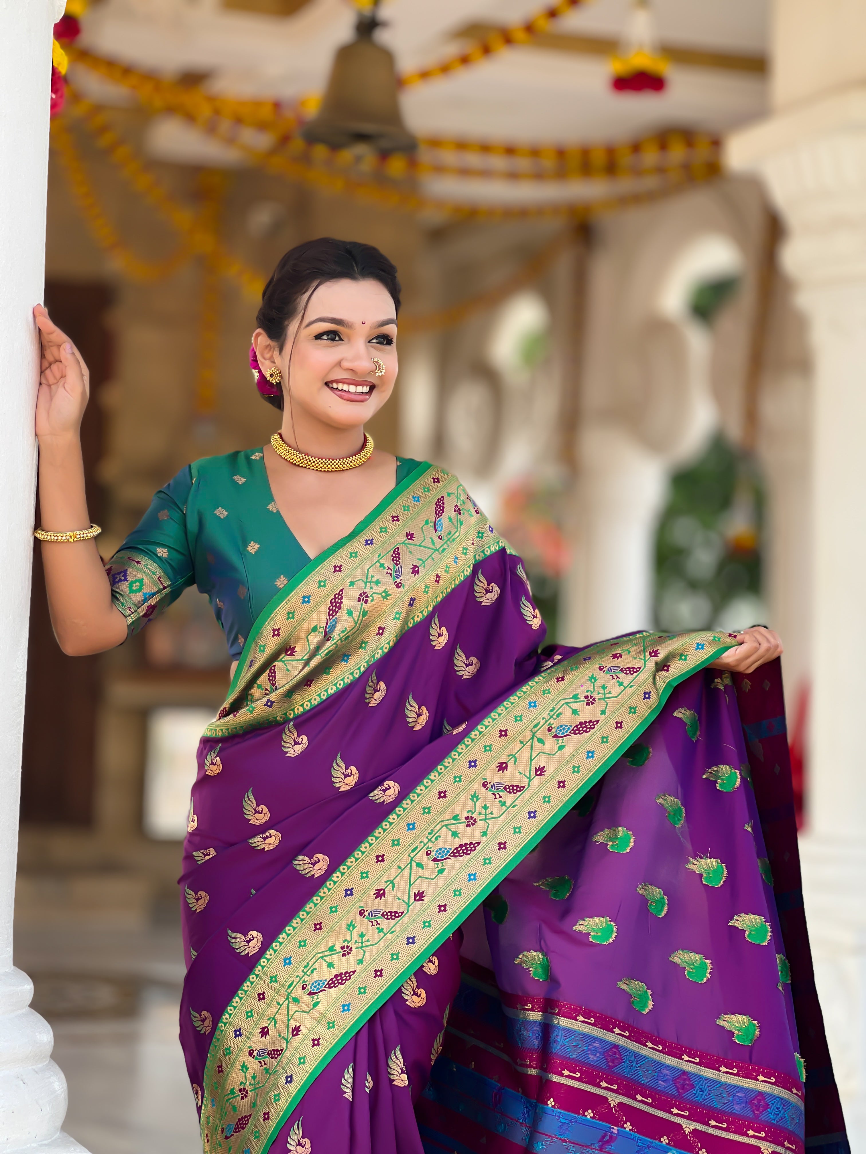 Woman wearing bottle Magenta soft Paithani silk saree with red Meenakari border and peacock zari motifs standing in a temple setting