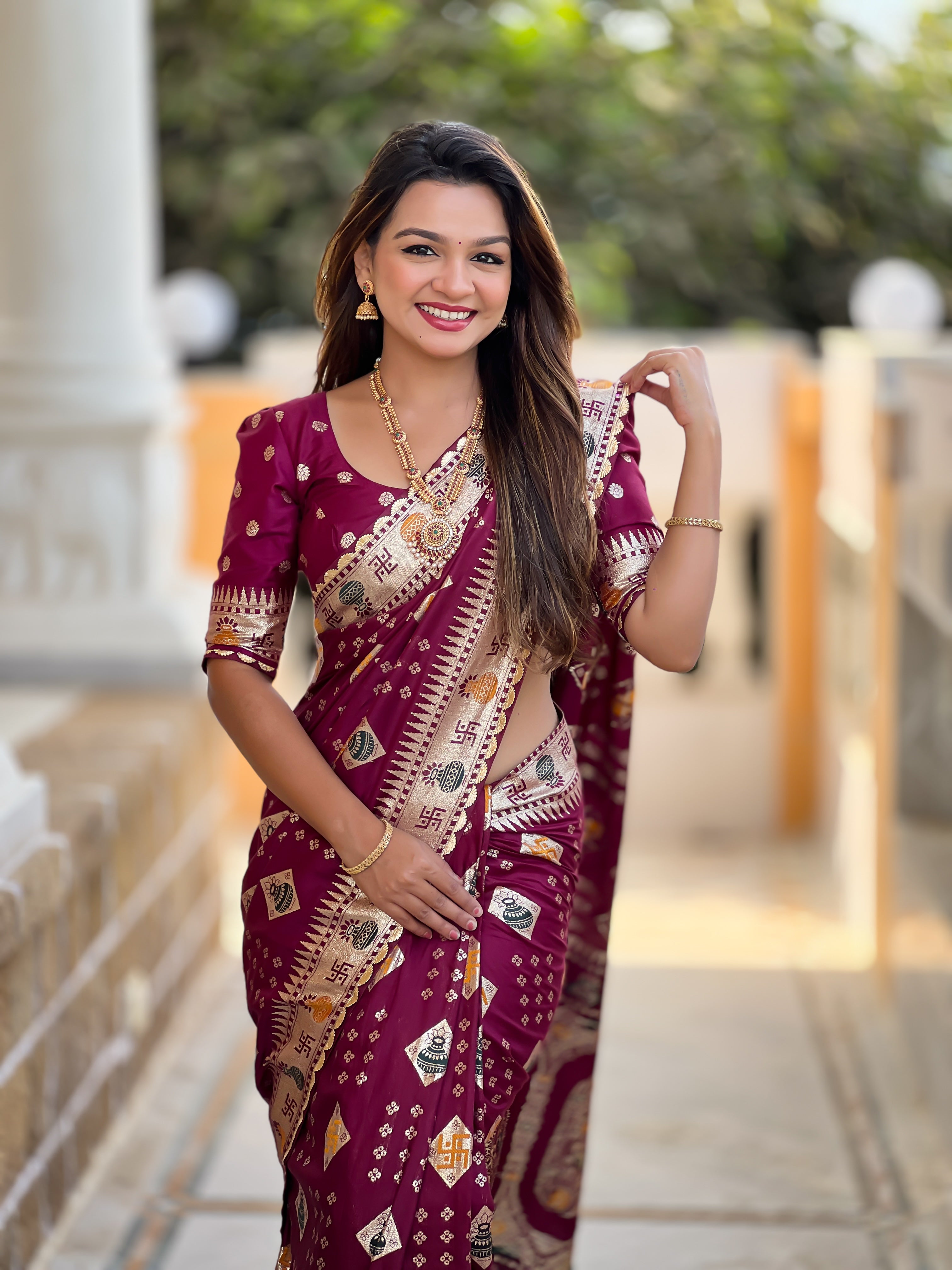 Woman wearing a maroon soft dola silk saree with gold zari and meenakari weaving, featuring a heavy pallu and tassels, ideal for indian weddings