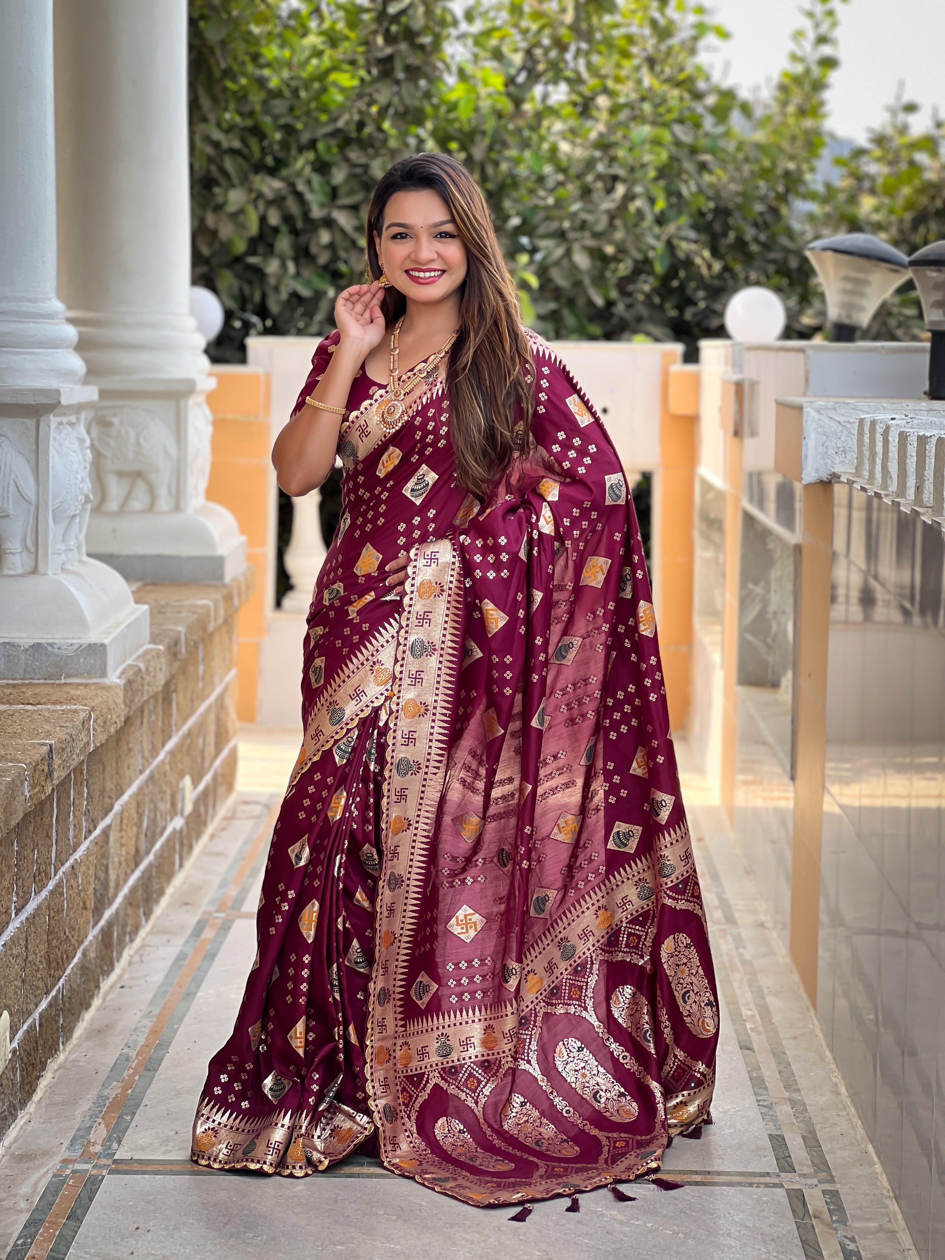 Woman wearing a maroon soft dola silk saree with gold zari and meenakari weaving, featuring a heavy pallu and tassels, ideal for indian weddings