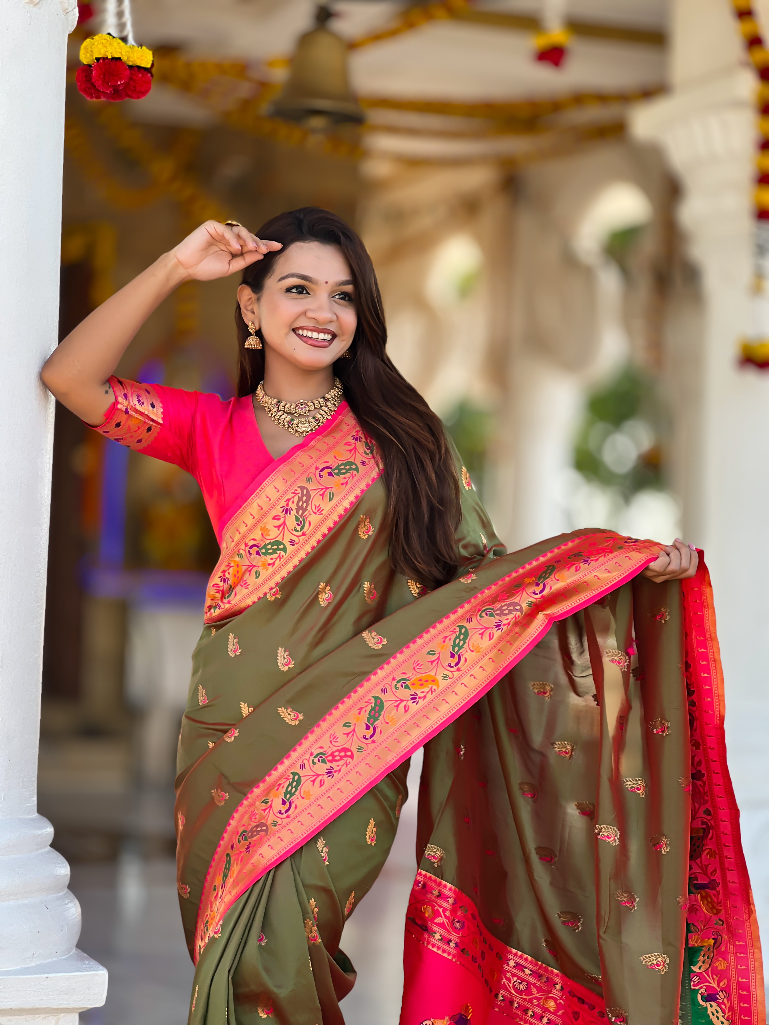 Model wearing a royal soft Paithani silk saree with Meenakari zari weaving and contrast pink border in a traditional temple setting