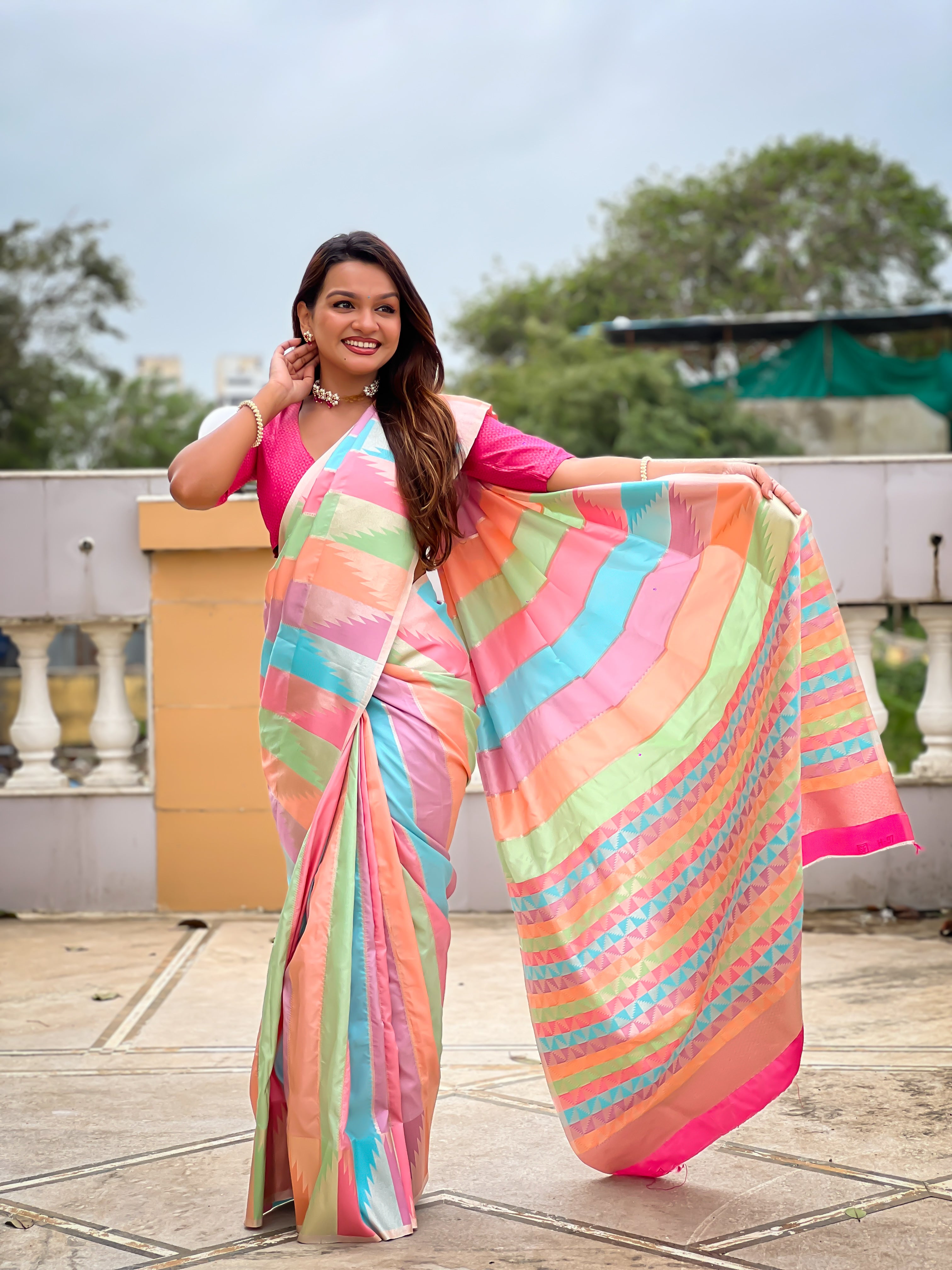 Woman wearing a multi-colored striped soft silk saree with Meenakari Zari weaving and a hot pink blouse in a traditional setting