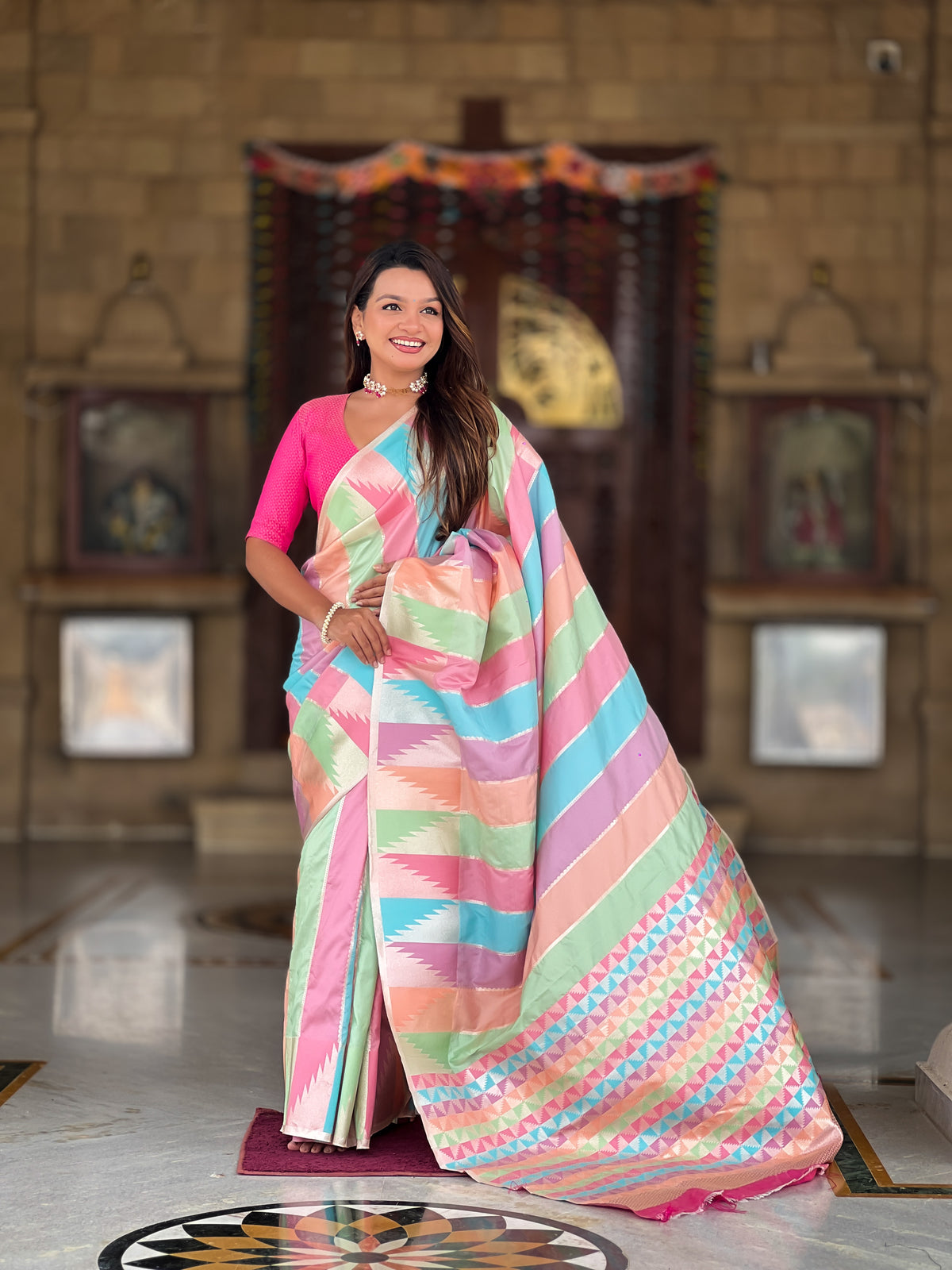 Woman wearing a multi-colored striped soft silk saree with Meenakari Zari weaving and a hot pink blouse in a traditional setting