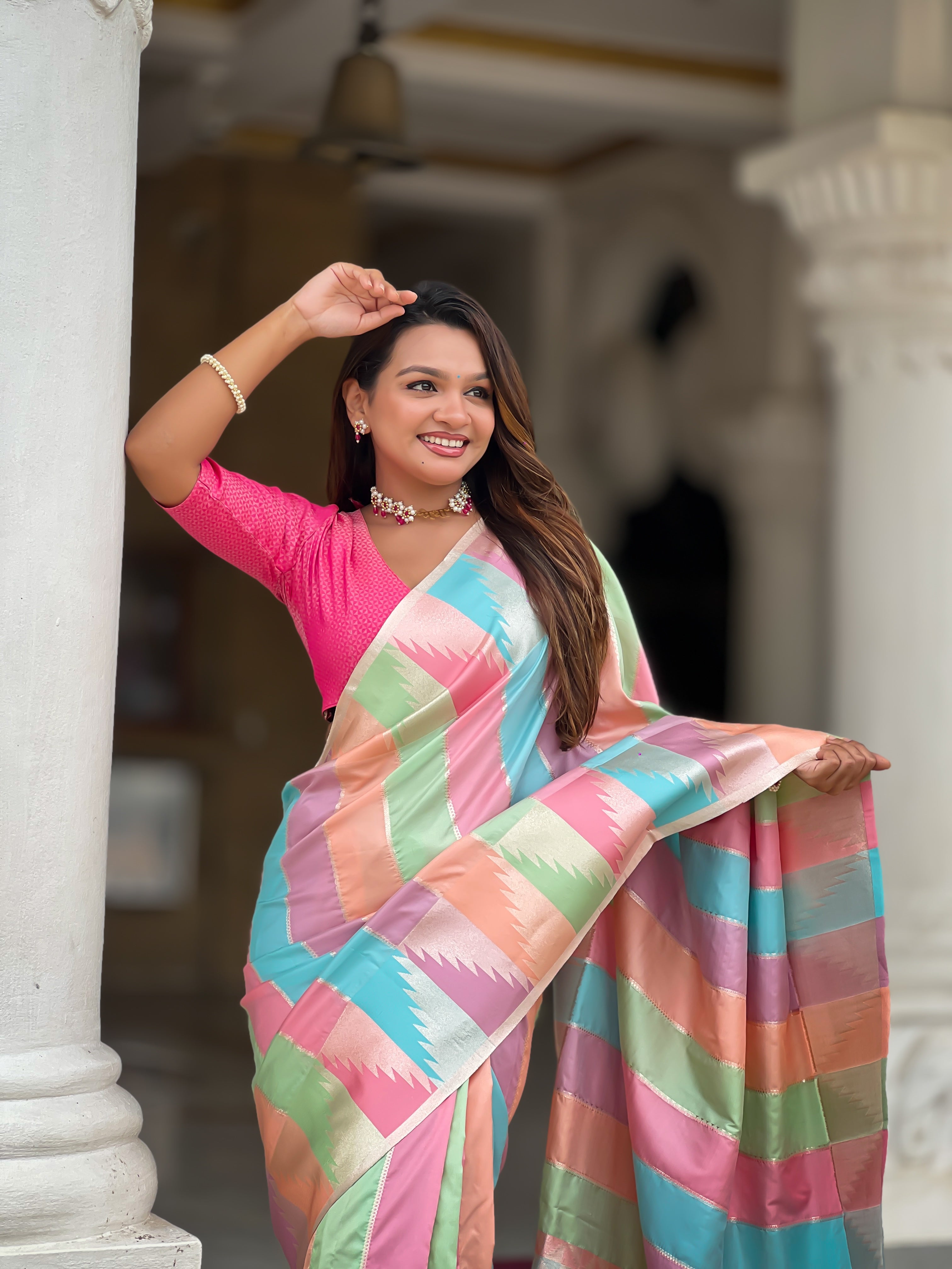 Woman wearing a multi-colored striped soft silk saree with Meenakari Zari weaving and a hot pink blouse in a traditional setting