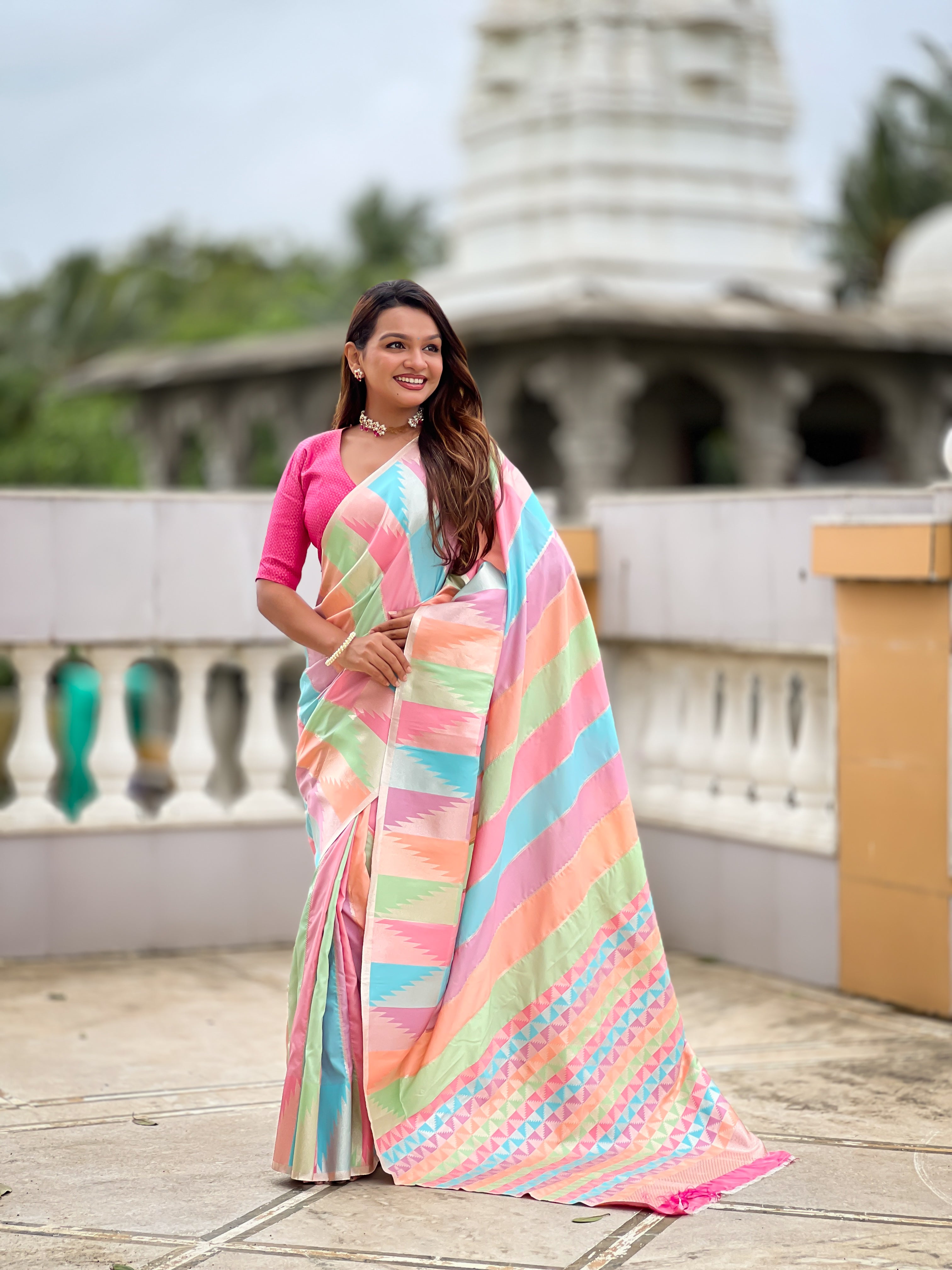 Woman wearing a multi-colored striped soft silk saree with Meenakari Zari weaving and a hot pink blouse in a traditional setting