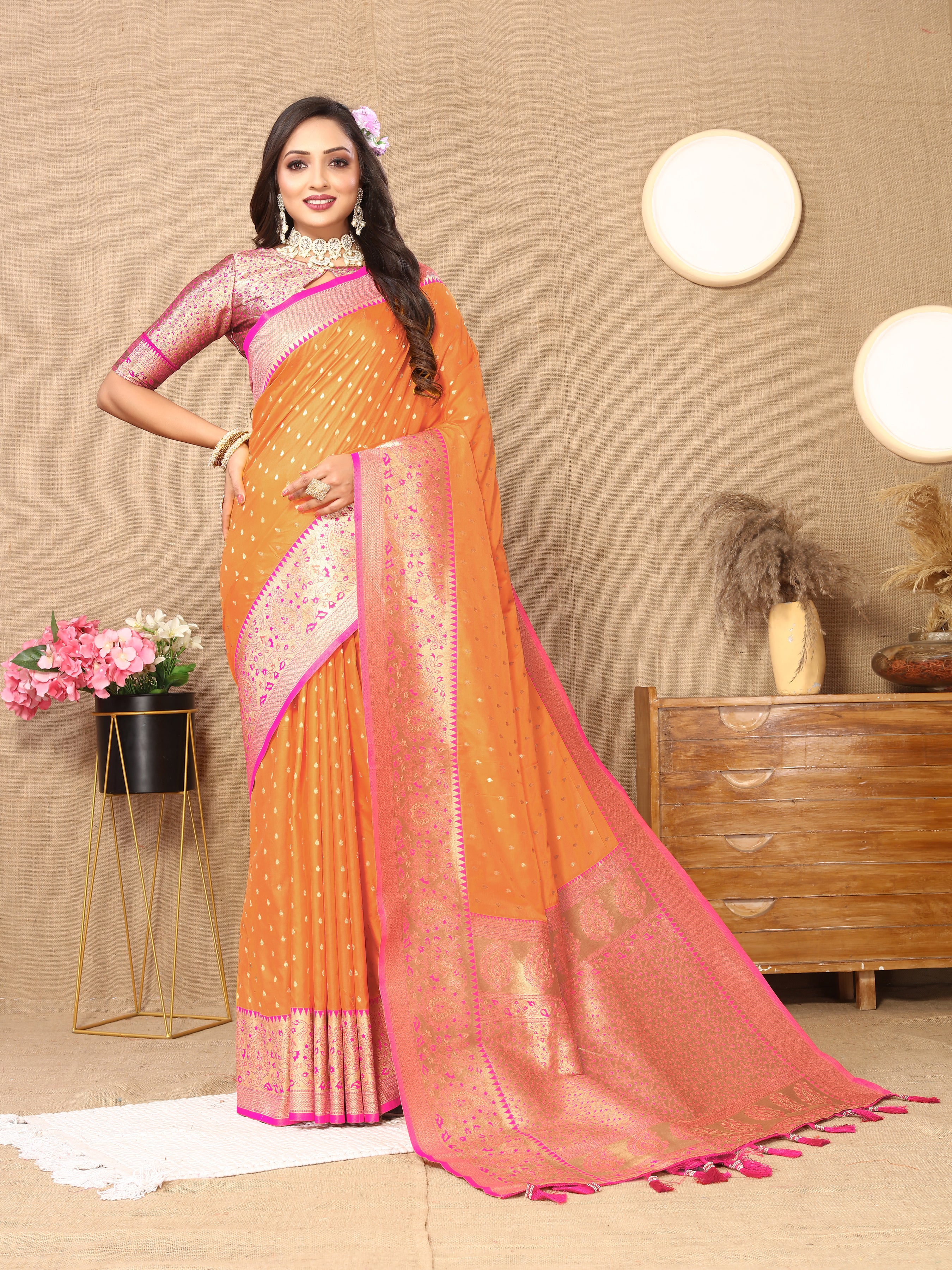 Woman wearing Orange soft silk saree with pink contrast border, gold zari motifs, and rich pallu design