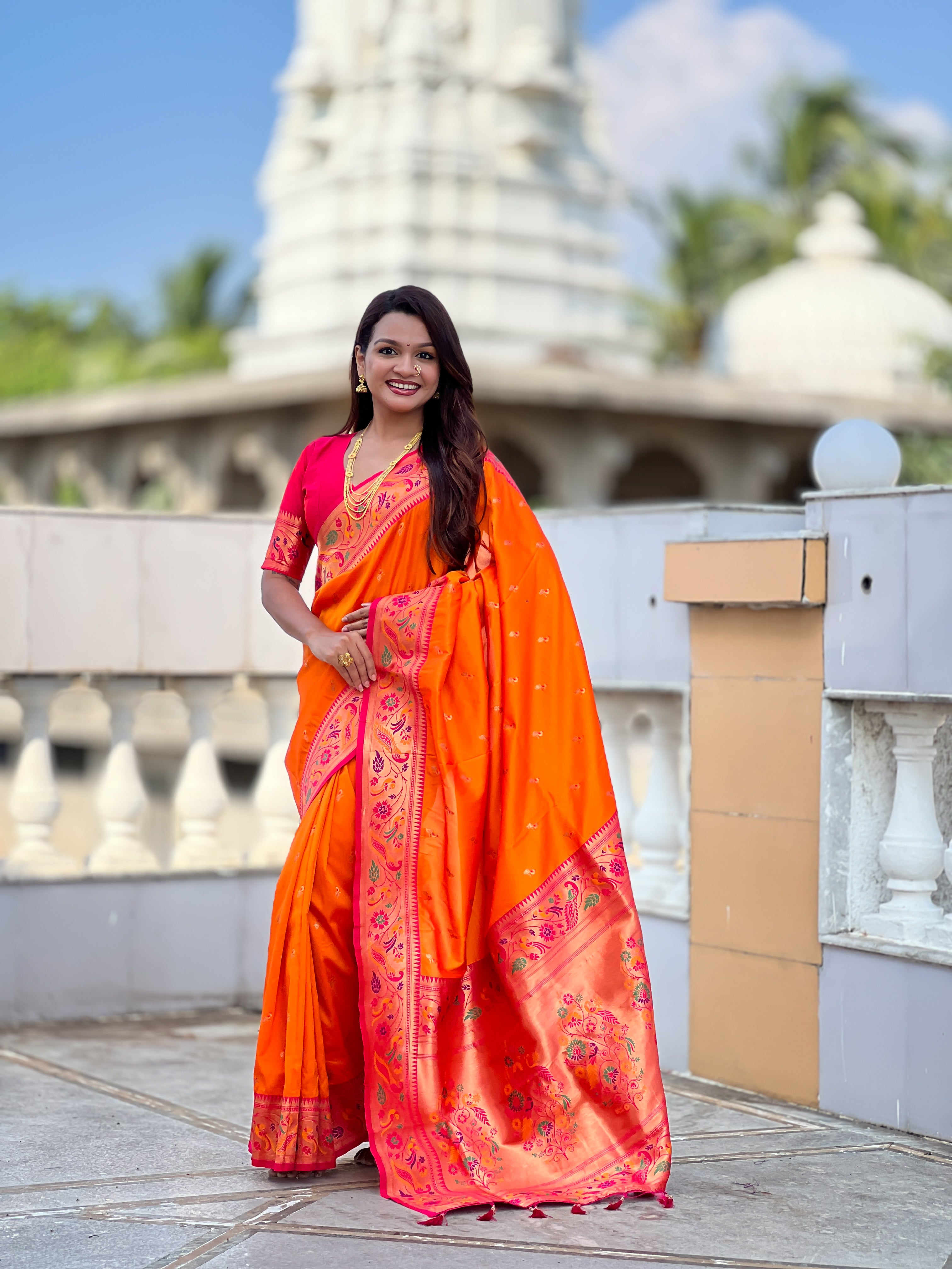 Woman wearing Orange Soft Paithani Silk Saree with pink border and Meenakari Zari weaving motifs