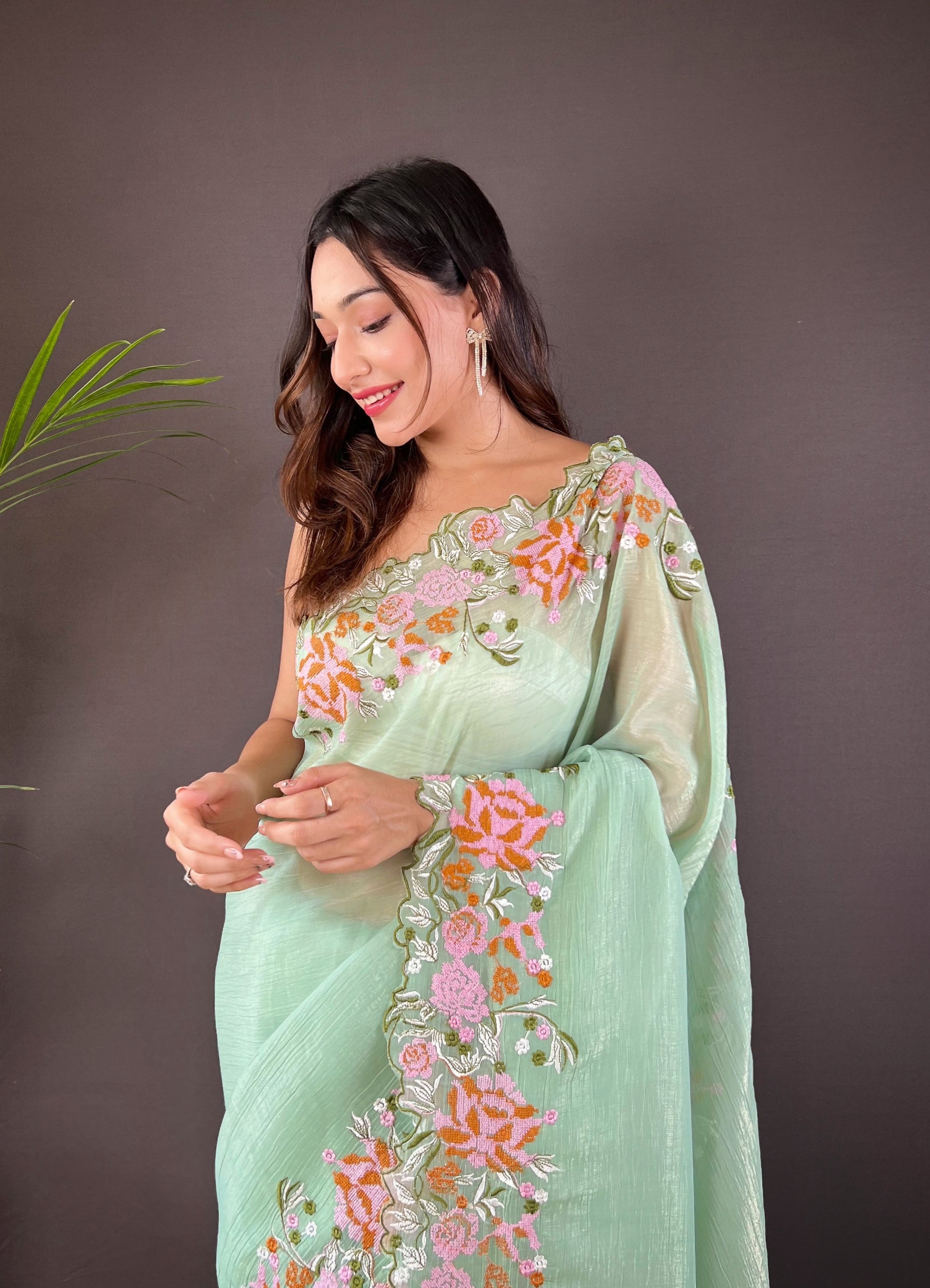 Woman wearing soft glossy silk saree with pink floral cross stitch embroidery and scalloped cutwork border