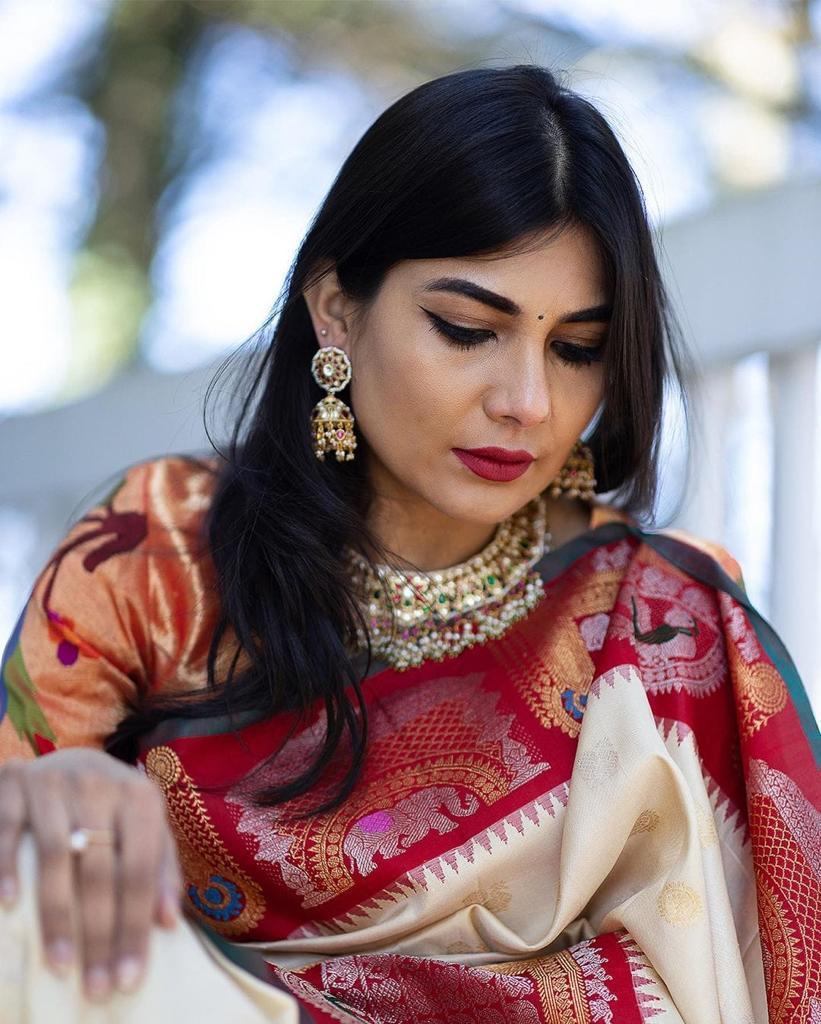 A woman wearing a traditional off-white and red Banarasi silk saree with gold jewelry.
