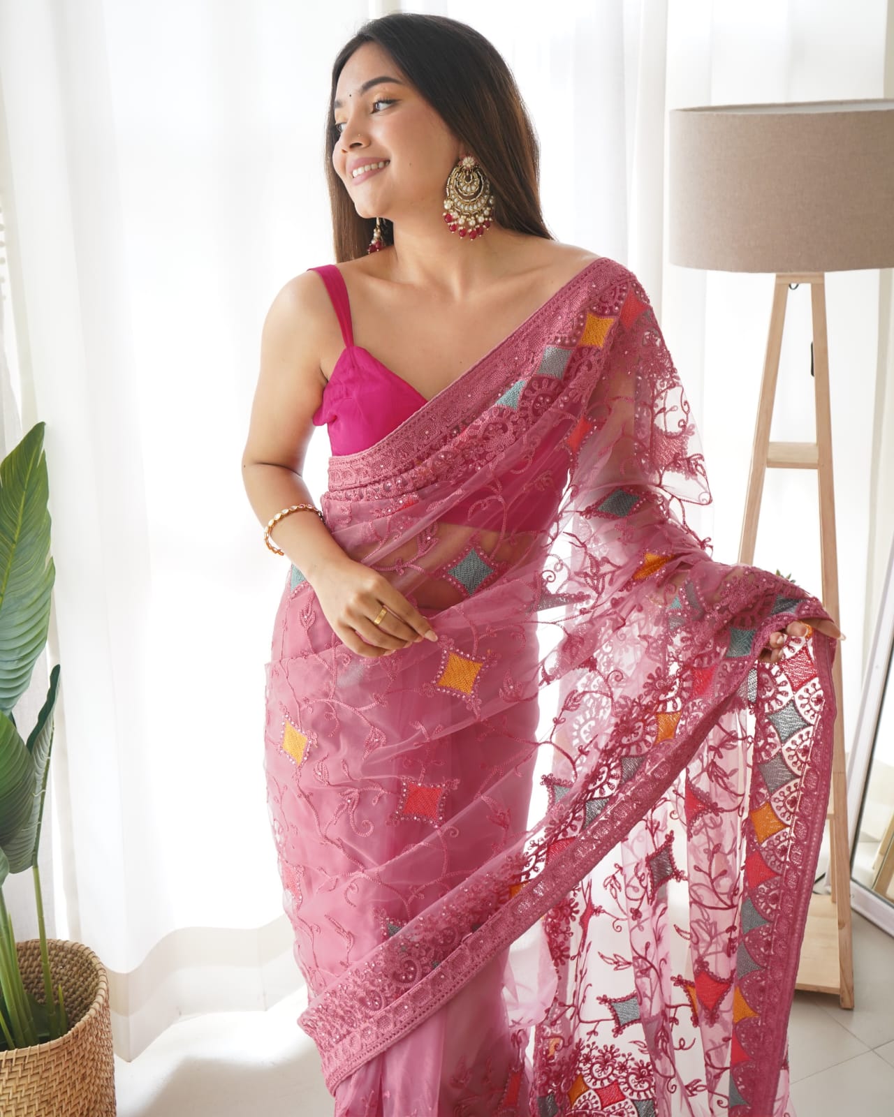Woman wearing pink heavy butterfly net saree with multi-color aari embroidery and stone work details