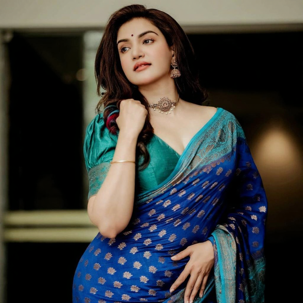 Royal blue Banarasi Silk saree with gold zari buttis and a teal contrast border, worn by a model in a natural light setting.